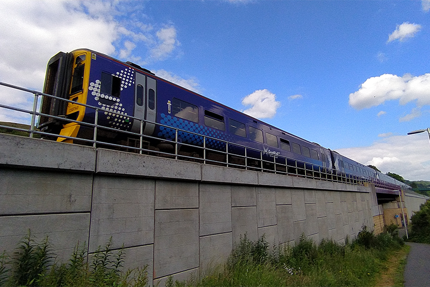 A construction view of the A6 Manchester Airport Relief Road project, showcasing a large retaining wall built using Geoquest Co. Ltd.'s precast concrete facing panels. The image highlights the integration of the road with surrounding infrastructure, illustrating the scale of the project and the innovative design solutions employed for the retaining walls and bridge abutments.
