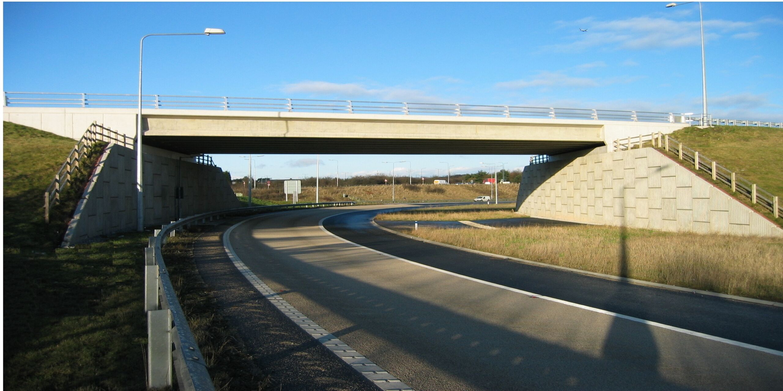 A construction view of the A6 Manchester Airport Relief Road project, showcasing a large retaining wall built using Geoquest Co. Ltd.'s precast concrete facing panels. The image highlights the integration of the road with surrounding infrastructure, illustrating the scale of the project and the innovative design solutions employed for the retaining walls and bridge abutments.