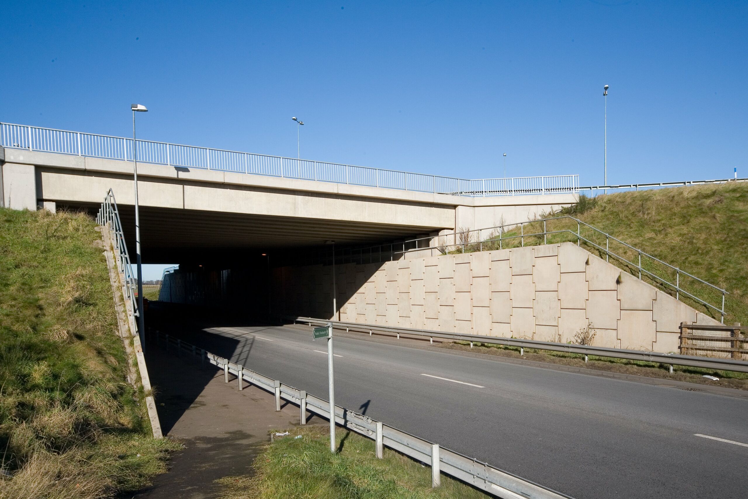 A construction view of the A6 Manchester Airport Relief Road project, showcasing a large retaining wall built using Geoquest Co. Ltd.'s precast concrete facing panels. The image highlights the integration of the road with surrounding infrastructure, illustrating the scale of the project and the innovative design solutions employed for the retaining walls and bridge abutments.