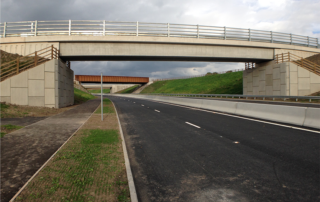A construction view of the A6 Manchester Airport Relief Road project, showcasing a large retaining wall built using Geoquest Co. Ltd.'s precast concrete facing panels. The image highlights the integration of the road with surrounding infrastructure, illustrating the scale of the project and the innovative design solutions employed for the retaining walls and bridge abutments.