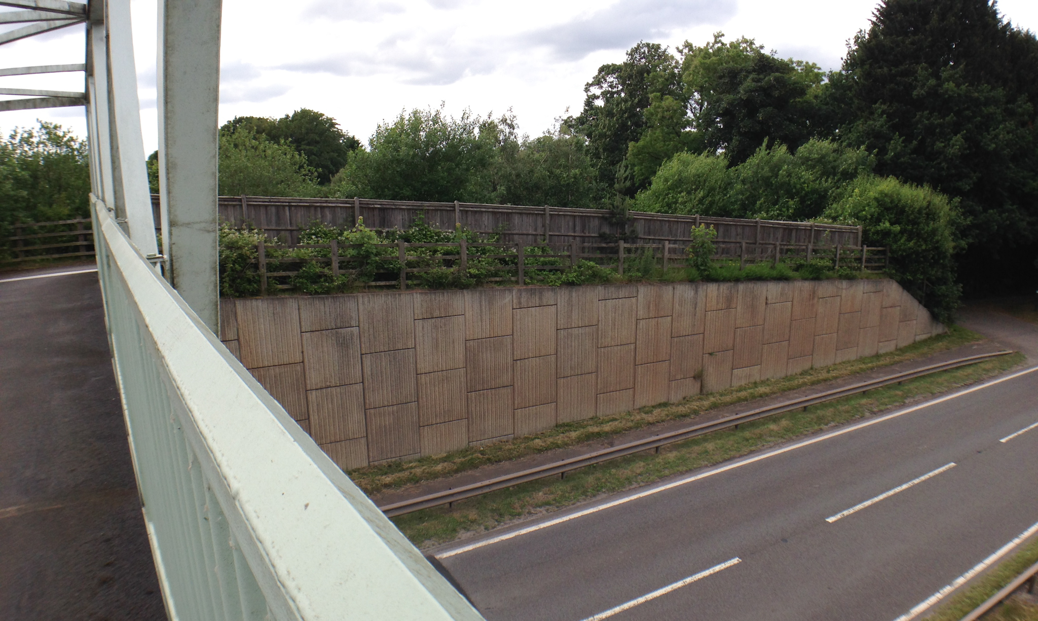 A construction view of the A6 Manchester Airport Relief Road project, showcasing a large retaining wall built using Geoquest Co. Ltd.'s precast concrete facing panels. The image highlights the integration of the road with surrounding infrastructure, illustrating the scale of the project and the innovative design solutions employed for the retaining walls and bridge abutments.