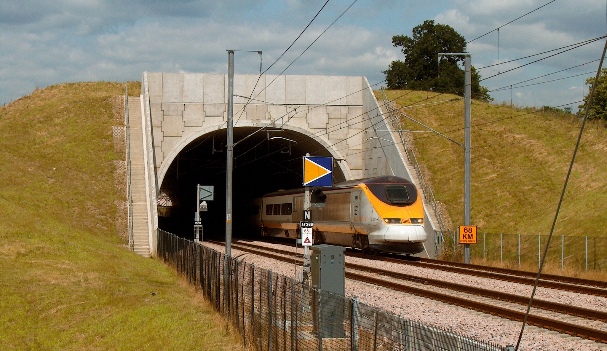 A construction view of the A6 Manchester Airport Relief Road project, showcasing a large retaining wall built using Geoquest Co. Ltd.'s precast concrete facing panels. The image highlights the integration of the road with surrounding infrastructure, illustrating the scale of the project and the innovative design solutions employed for the retaining walls and bridge abutments.