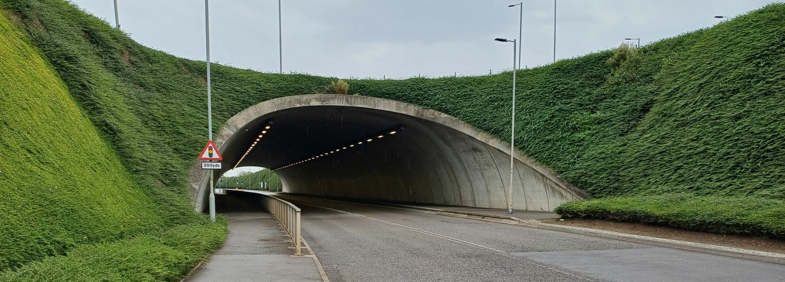 Vegetated Cut‑and‑Cover Tunnel Entrance near Heathrow Airport, UK Roadway approaching a Geoquest precast concrete cut‑and‑cover tunnel surrounded by steep vegetated embankments used in UK transport infrastructure.