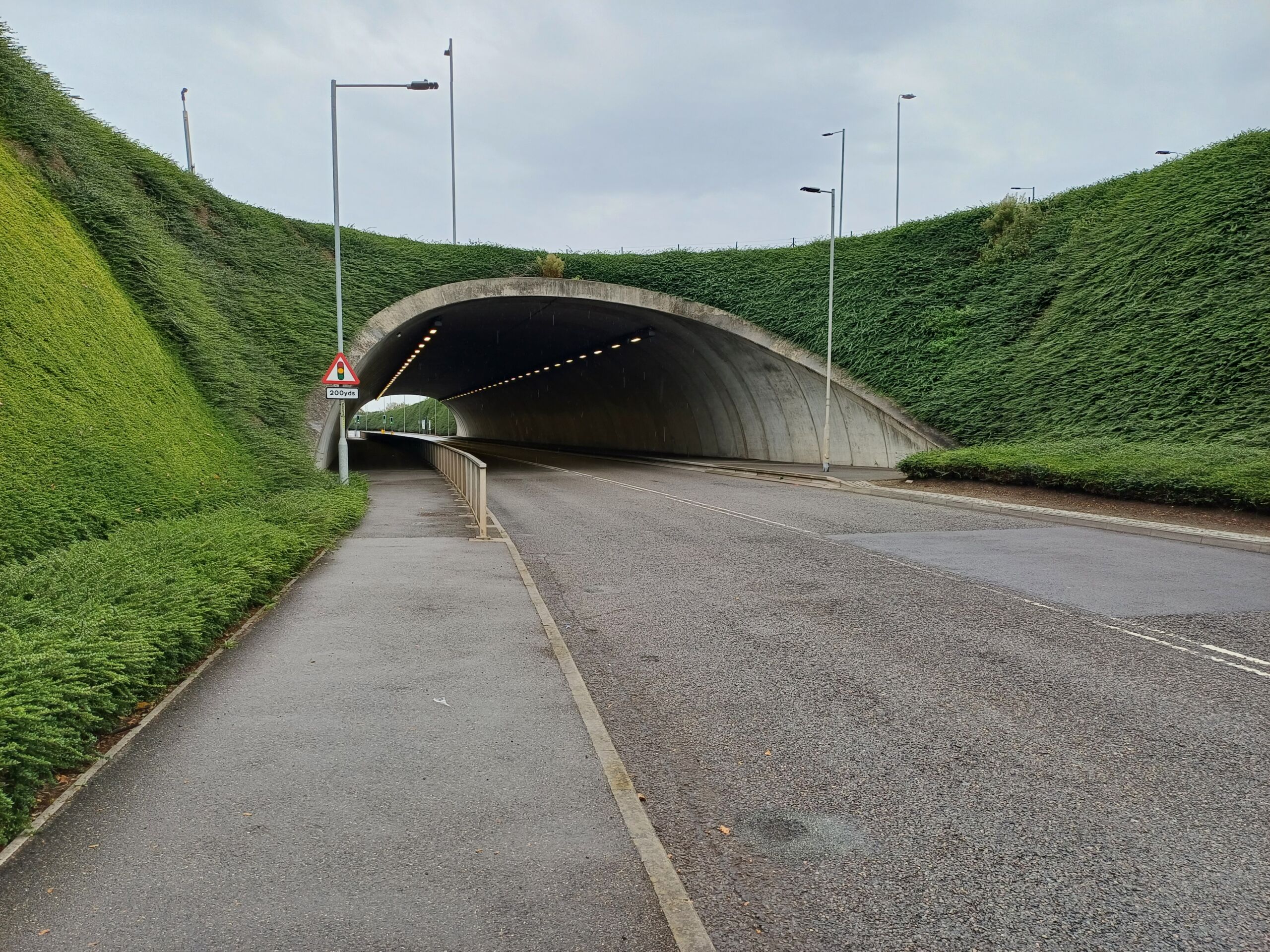 Roadway approaching a Geoquest precast concrete cut‑and‑cover tunnel surrounded by steep vegetated embankments used in UK transport infrastructure.
